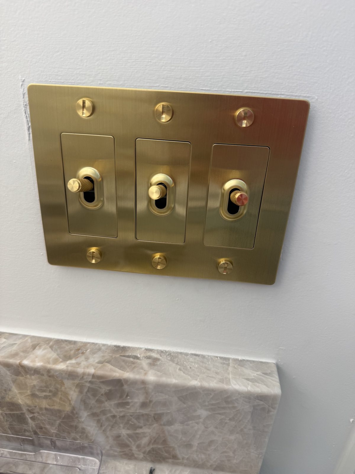 Designer brass switch plate and toggles, cleanly trimmed.